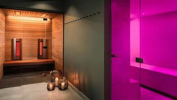 Ett modernt spa-rum med träpanel, uppvärmt golv och en bastu med rosa belysning.
