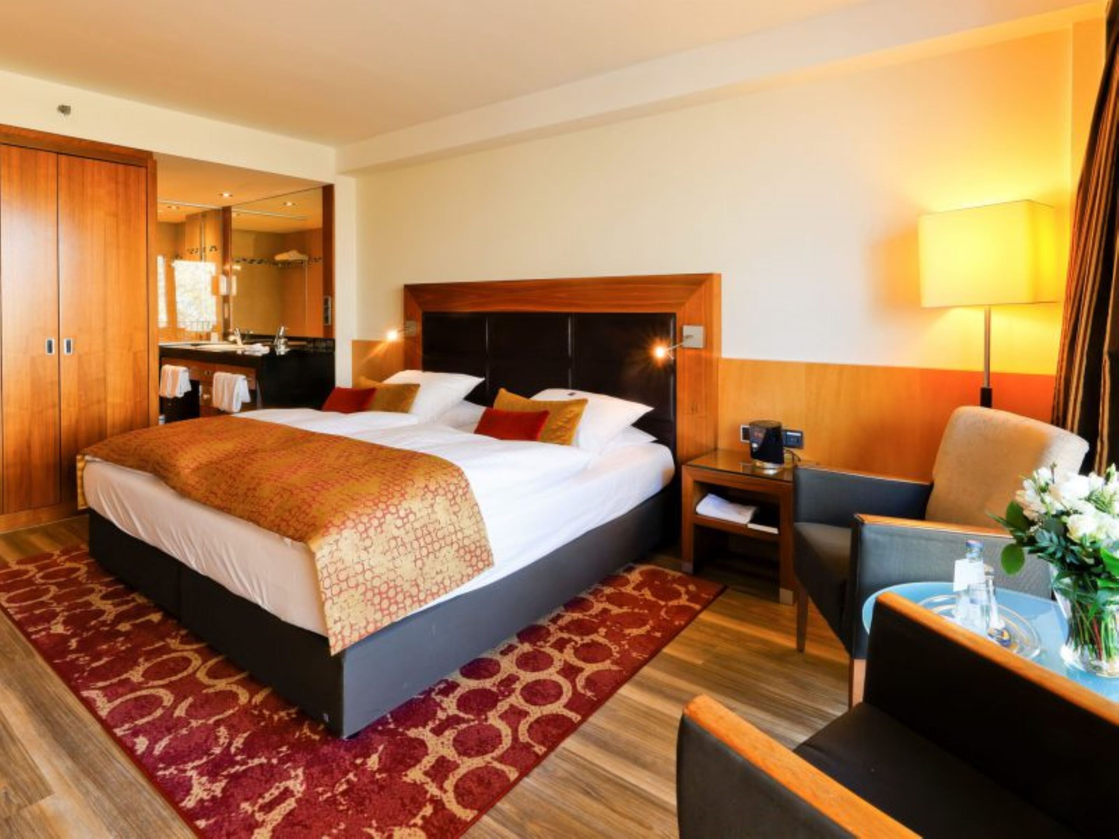 A hotel room with a large bed, a desk, a chair, and a small table with a vase of flowers.