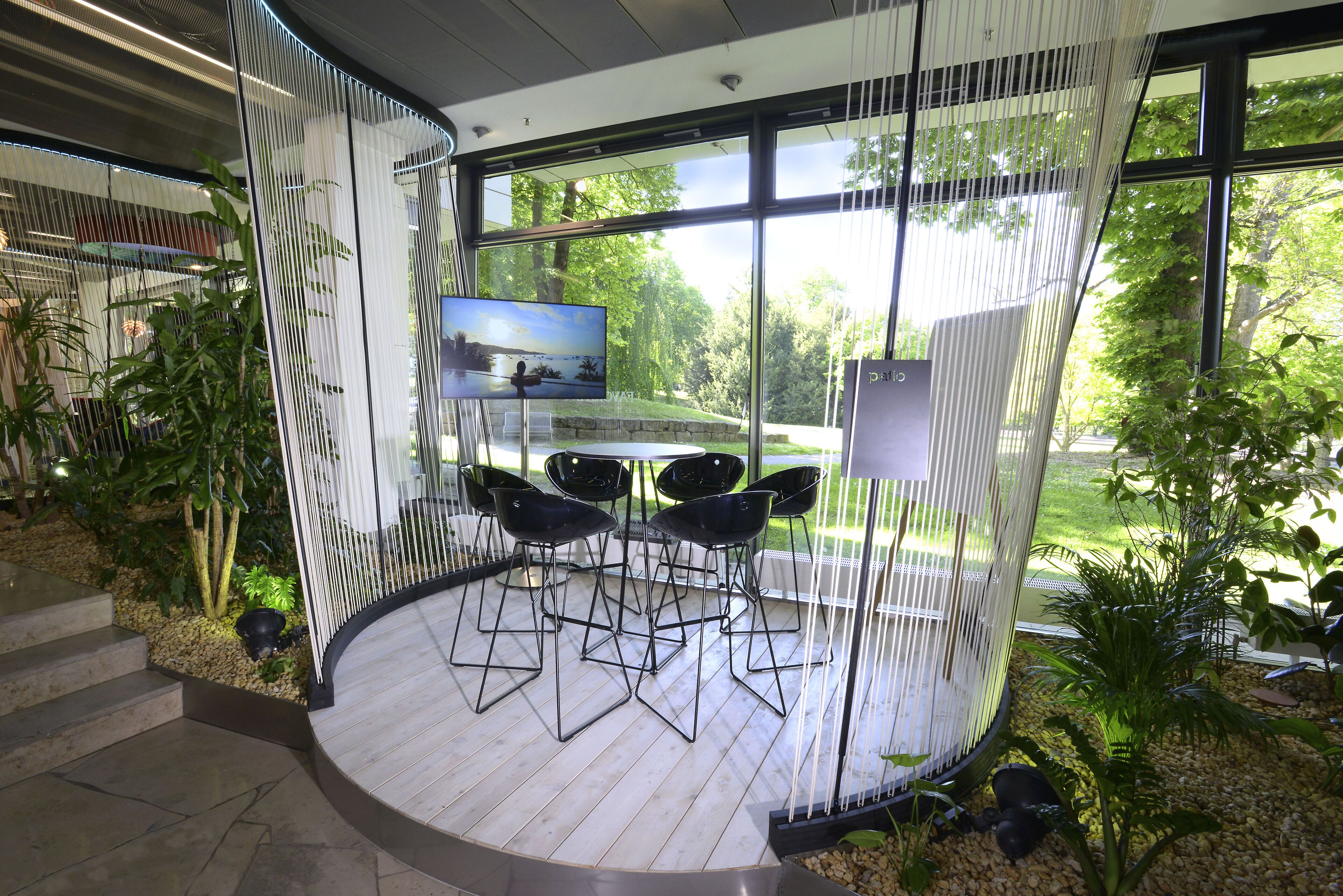 Un espace intérieur moderne doté d’un coin salon circulaire, d’un téléviseur à écran plat et de grandes fenêtres offrant une vue sur la verdure environnante.