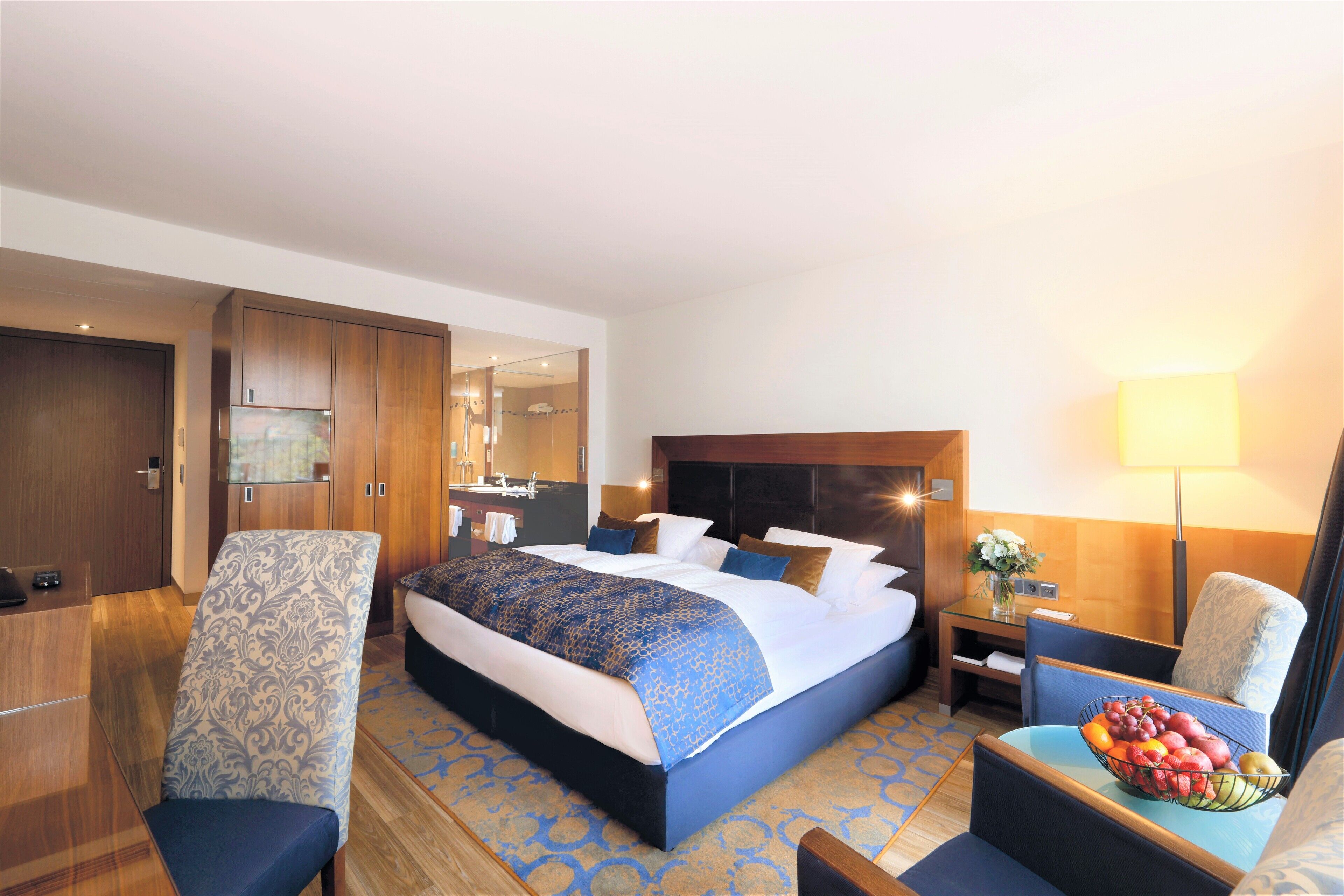 A hotel room with a large bed, a desk, a chair, a nightstand, and a fruit bowl.