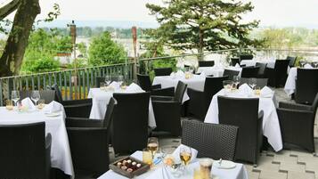 An outdoor dining area with wicker chairs and white tablecloths, set against a scenic backdrop.