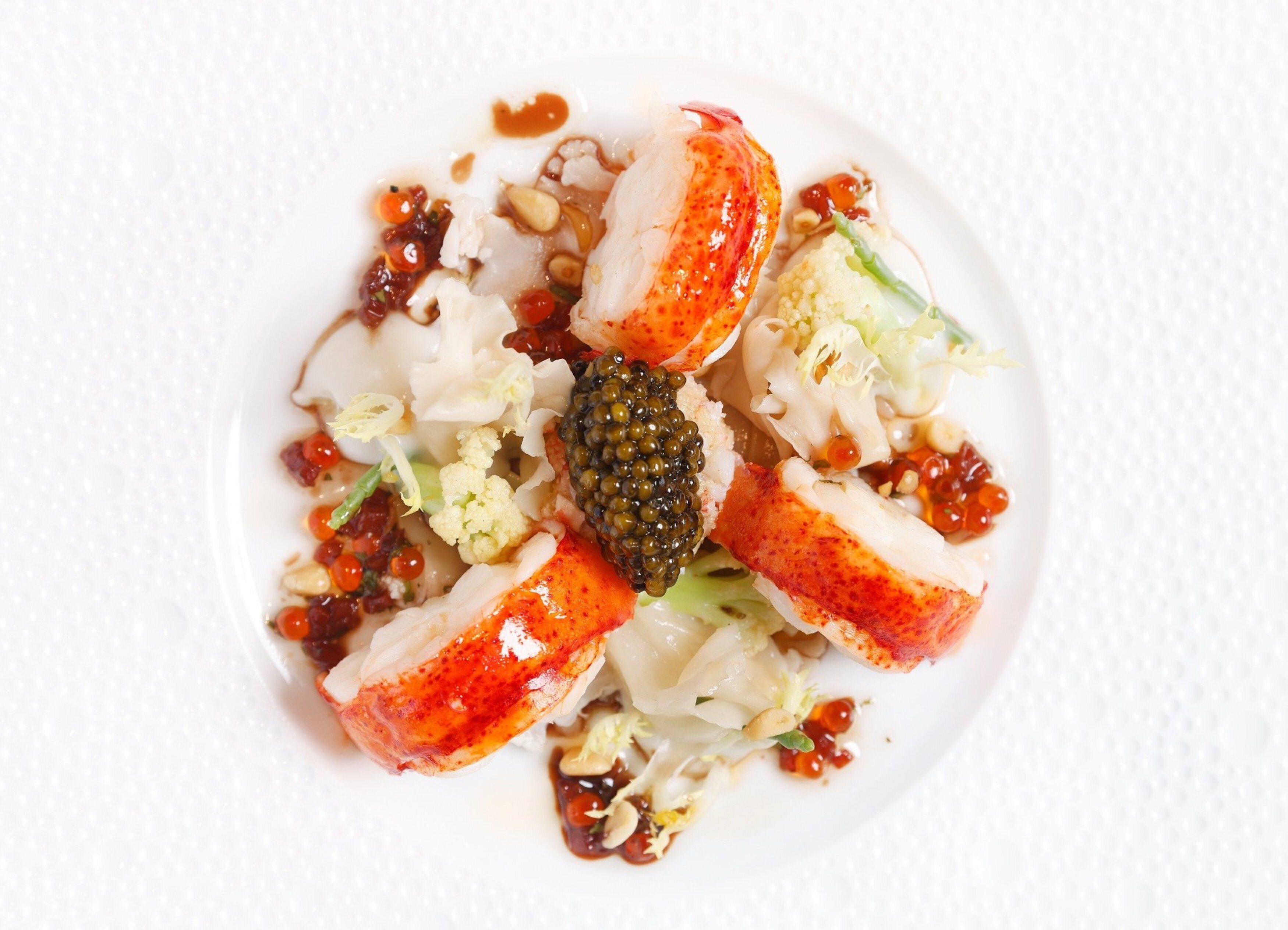 Un piatto di cibo con aragosta, caviale e verdure.