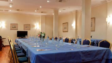 Une salle de conférence avec une longue table préparée pour une réunion, équipée de chaises et d’un téléviseur.