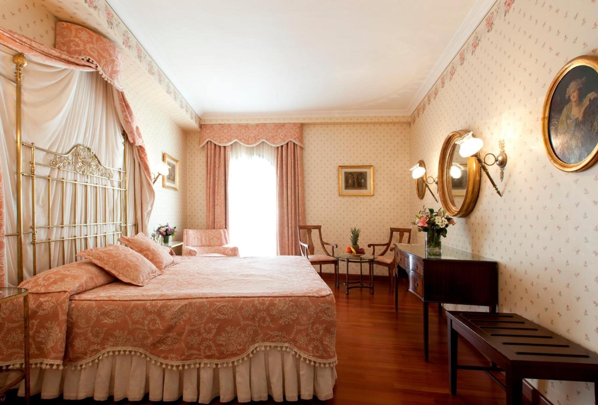 Una habitación con una cama grande, dos sillas, una mesita con flores y un espejo en la pared.