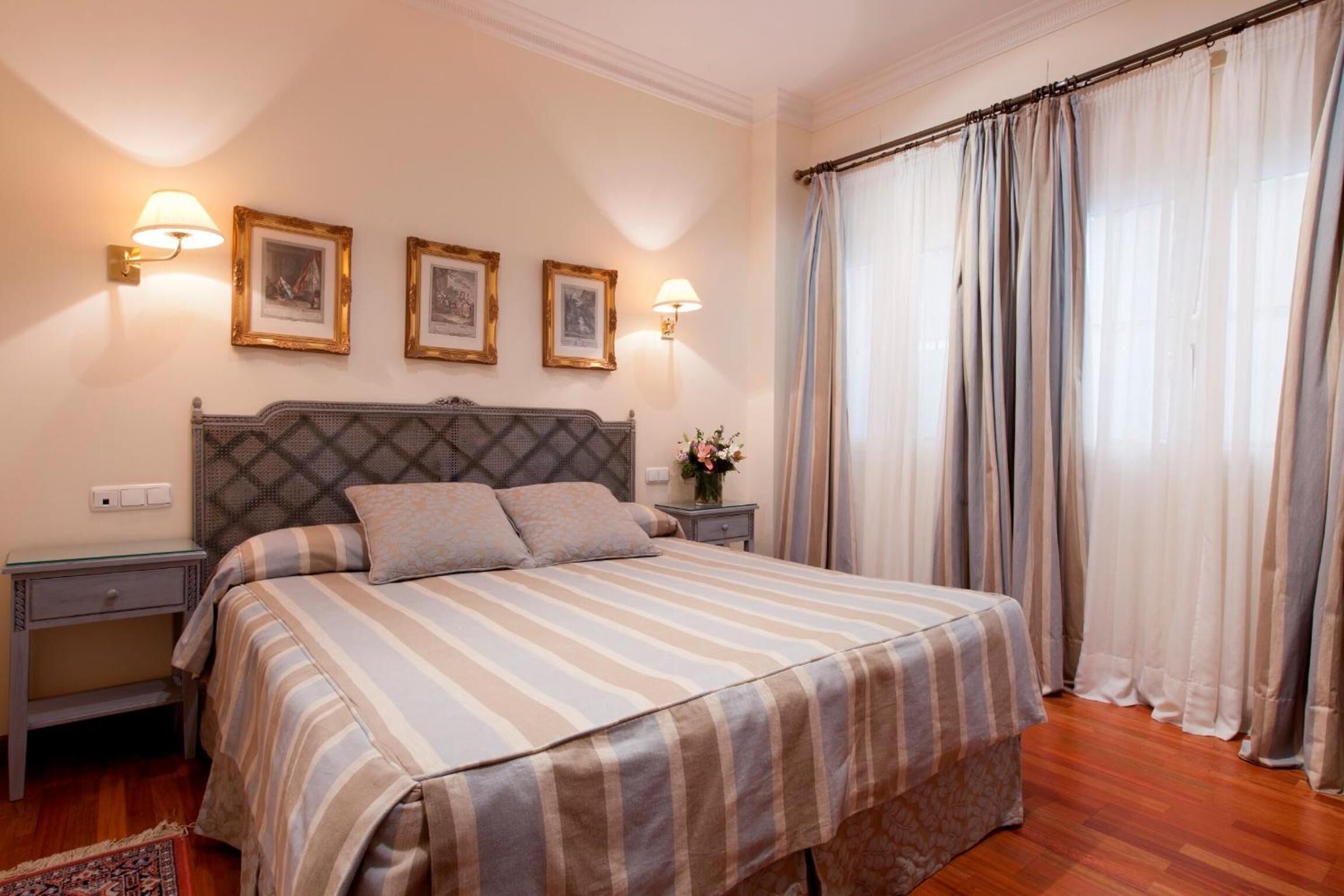 Een netjes opgemaakt slaapkamer met een bed, nachtkastjes en wandlampen.