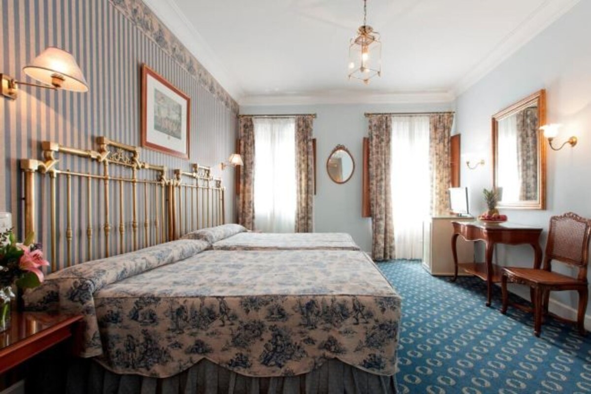 A hotel room with two beds, a desk, and a chair.