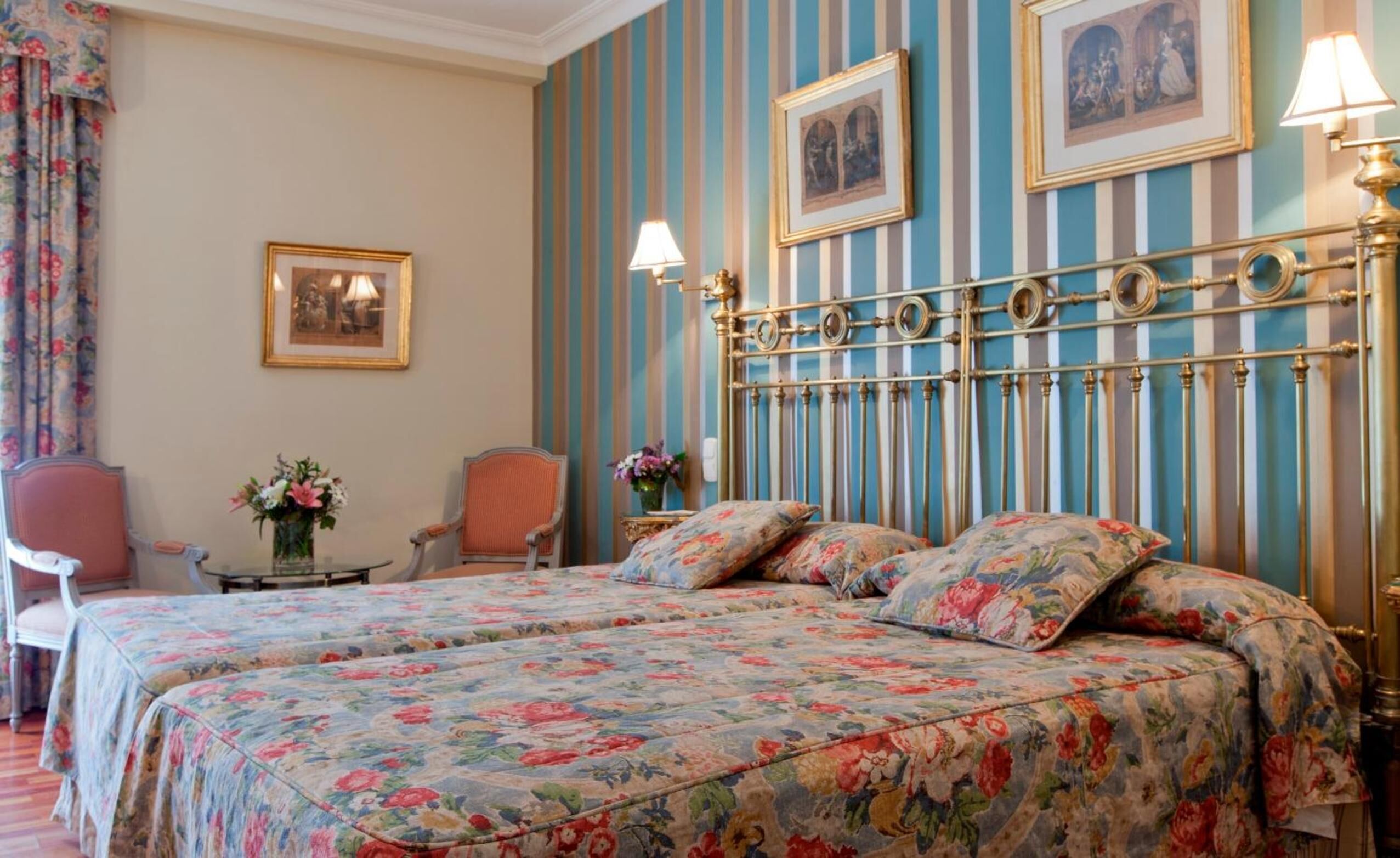 Une chambre d’hôtel avec un lit double, une couvre-lit à motifs floraux, un papier peint à rayures et deux tableaux encadrés accrochés au mur.