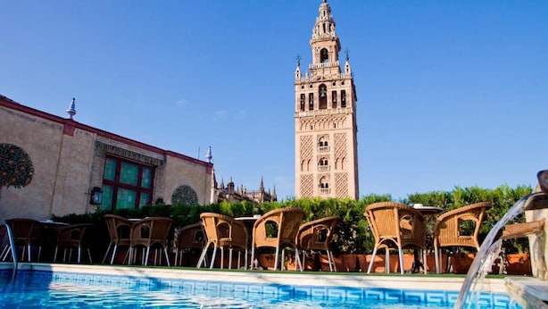 A pool area with lounge chairs and a view of a historic tower. - Hotel Doña Maria (Seville)