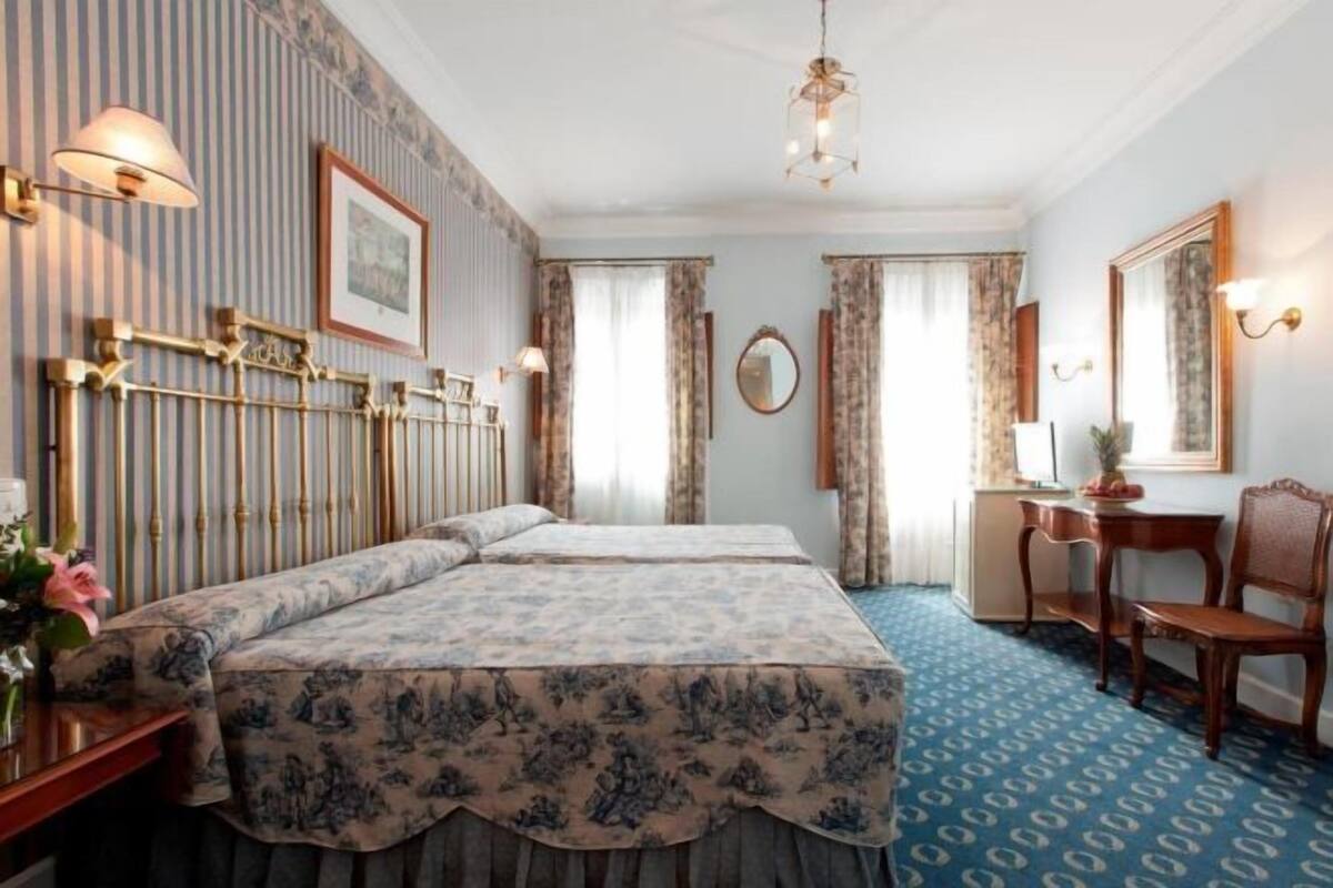 A hotel room with two beds, a desk, a chair, a mirror, and a patterned carpet.