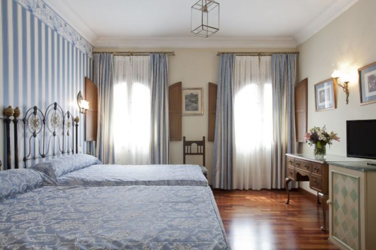 A hotel room with a double bed, a desk with a TV, and a cabinet.