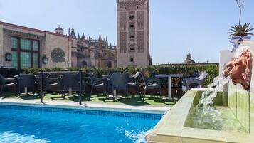 A swimming pool with lounge chairs and a fountain, with a historic tower in the background.