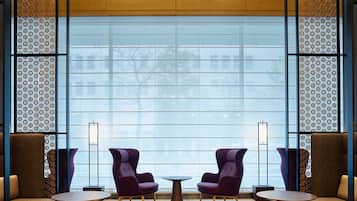 Un hall d’entrée moderne avec deux fauteuils violets, une petite table et une grande fenêtre donnant sur des immeubles.