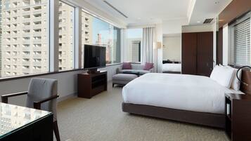 A hotel room with a large bed, a television, a desk, and a view of high-rise buildings.