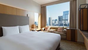 A hotel room with a large bed, a sofa, a small table, and a view of a cityscape.