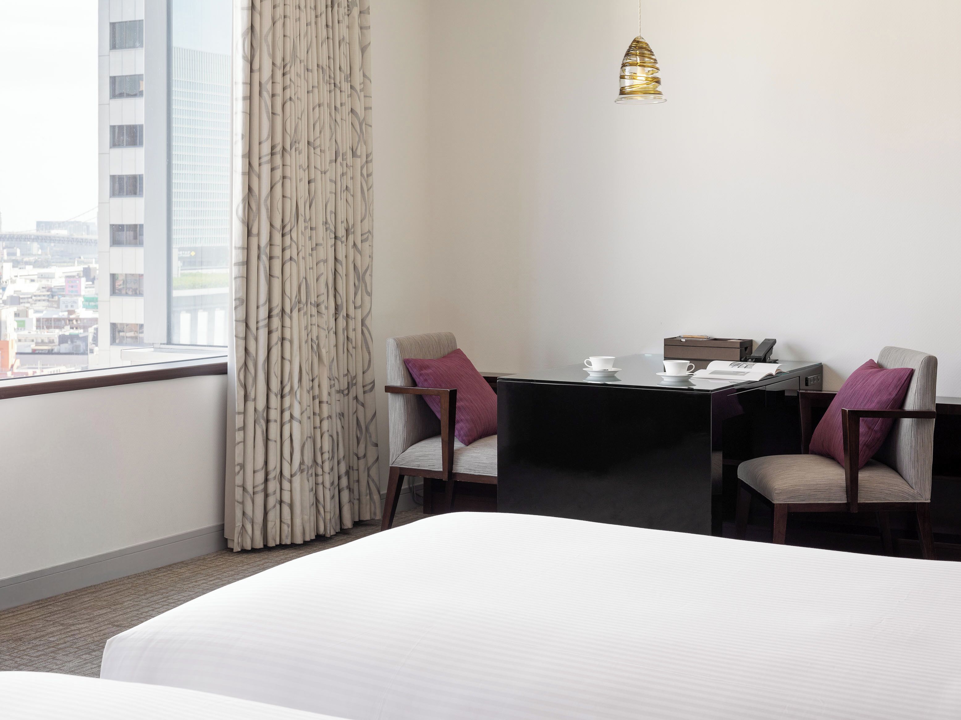 Habitación de hotel con una cama, un escritorio con dos sillas, una mesa con dos tazas y una lámpara colgante.