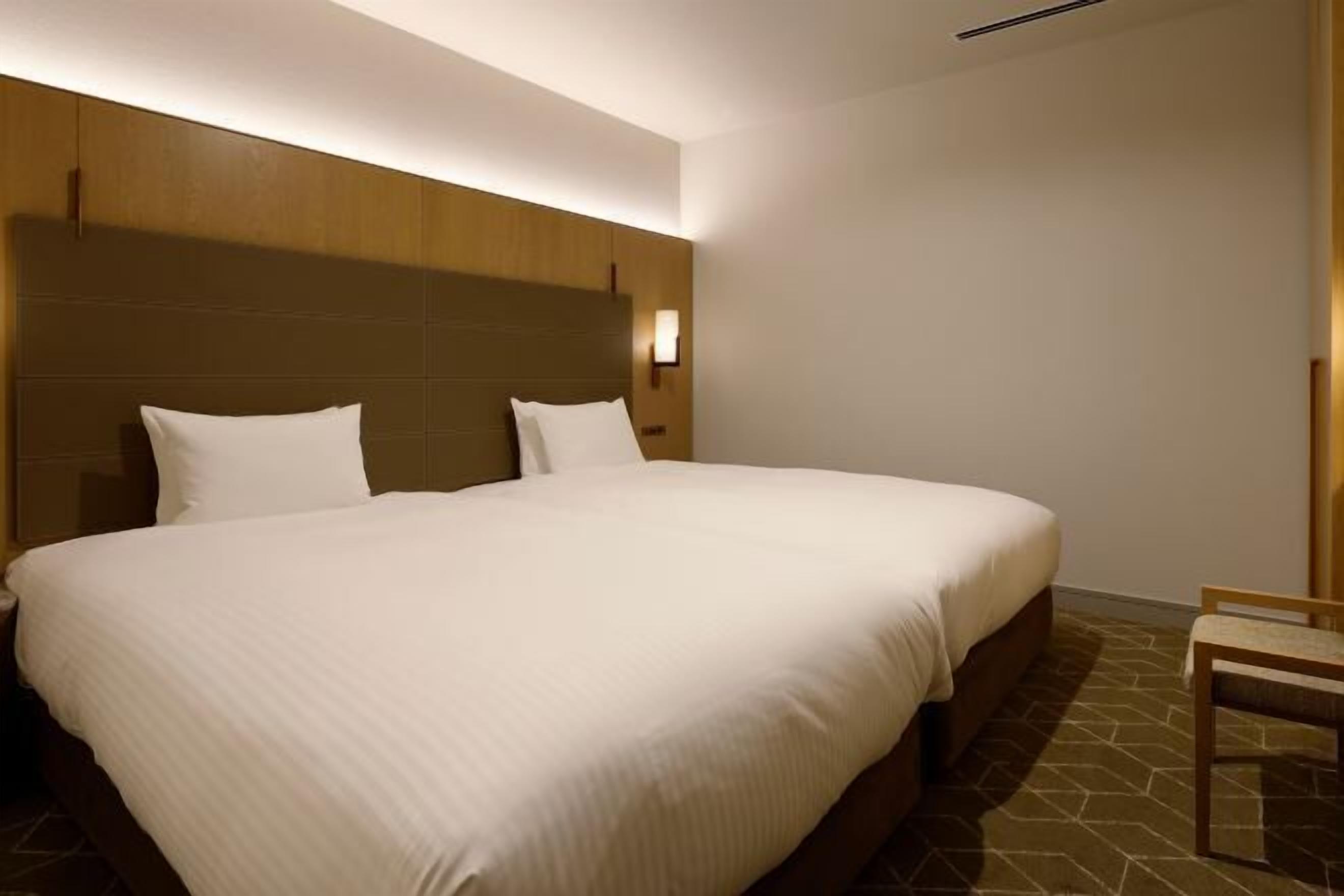 A hotel room with a large bed, a wooden headboard, a nightstand, and a chair.