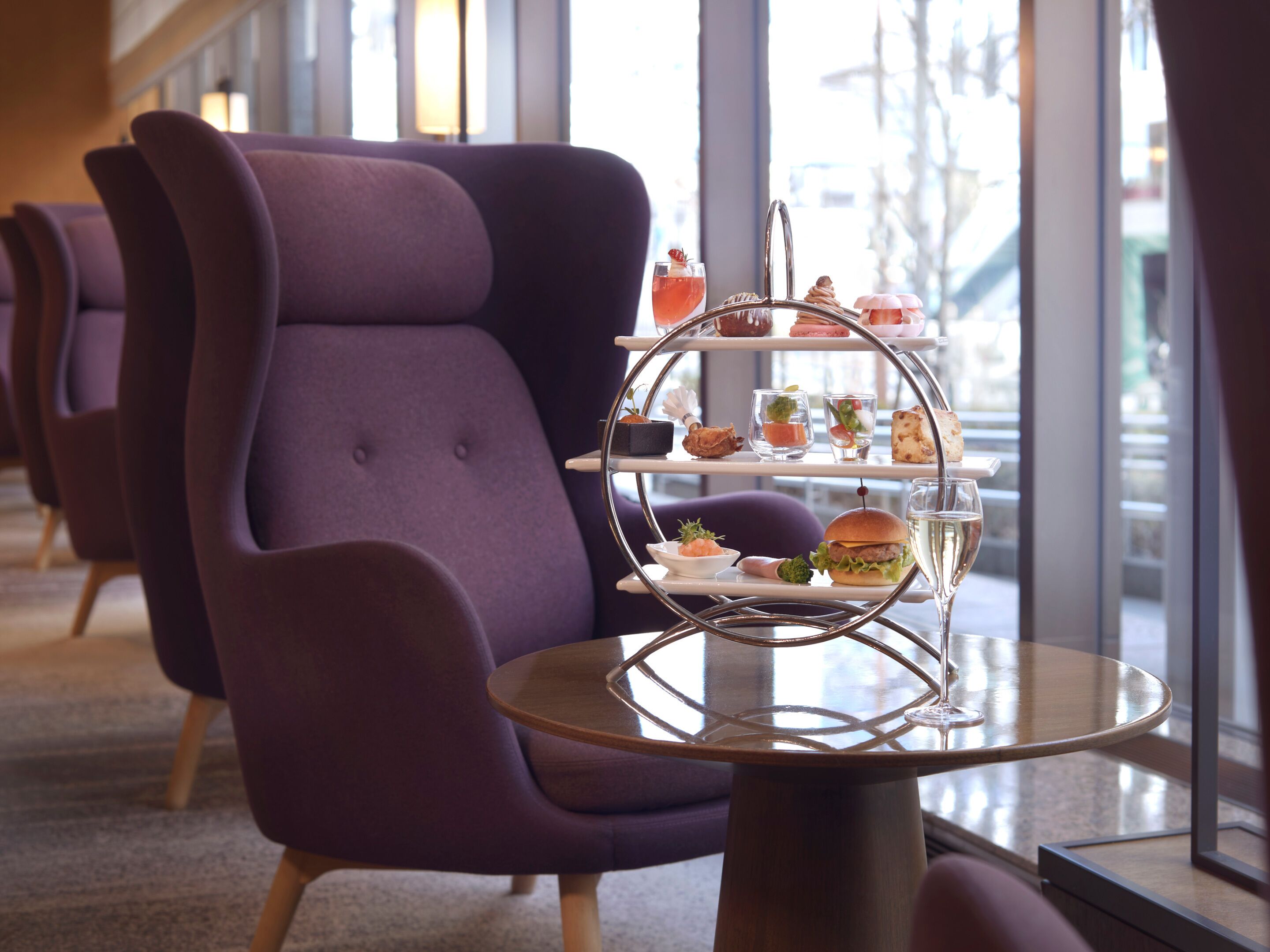 Un espace détente avec des chaises violettes et une table sur laquelle se trouve un présentoir à étages contenant des plats et des boissons.