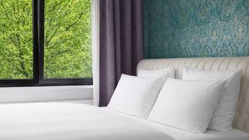 A bed with white linens, a window with a view of trees, and a patterned wall.