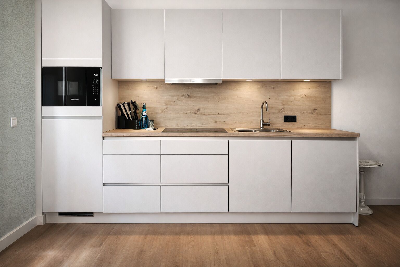 Una cocina moderna con armarios blancos, un microondas integrado, un lavamanos de acero inoxidable y una encimera de madera.
