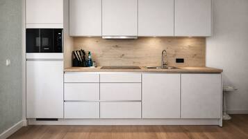 Una cocina moderna con armarios blancos, un microondas integrado, un lavamanos de acero inoxidable y una encimera de madera.