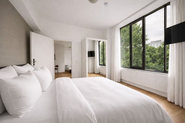 A modern hotel room with a large bed, a view of greenery, and a separate bathroom.