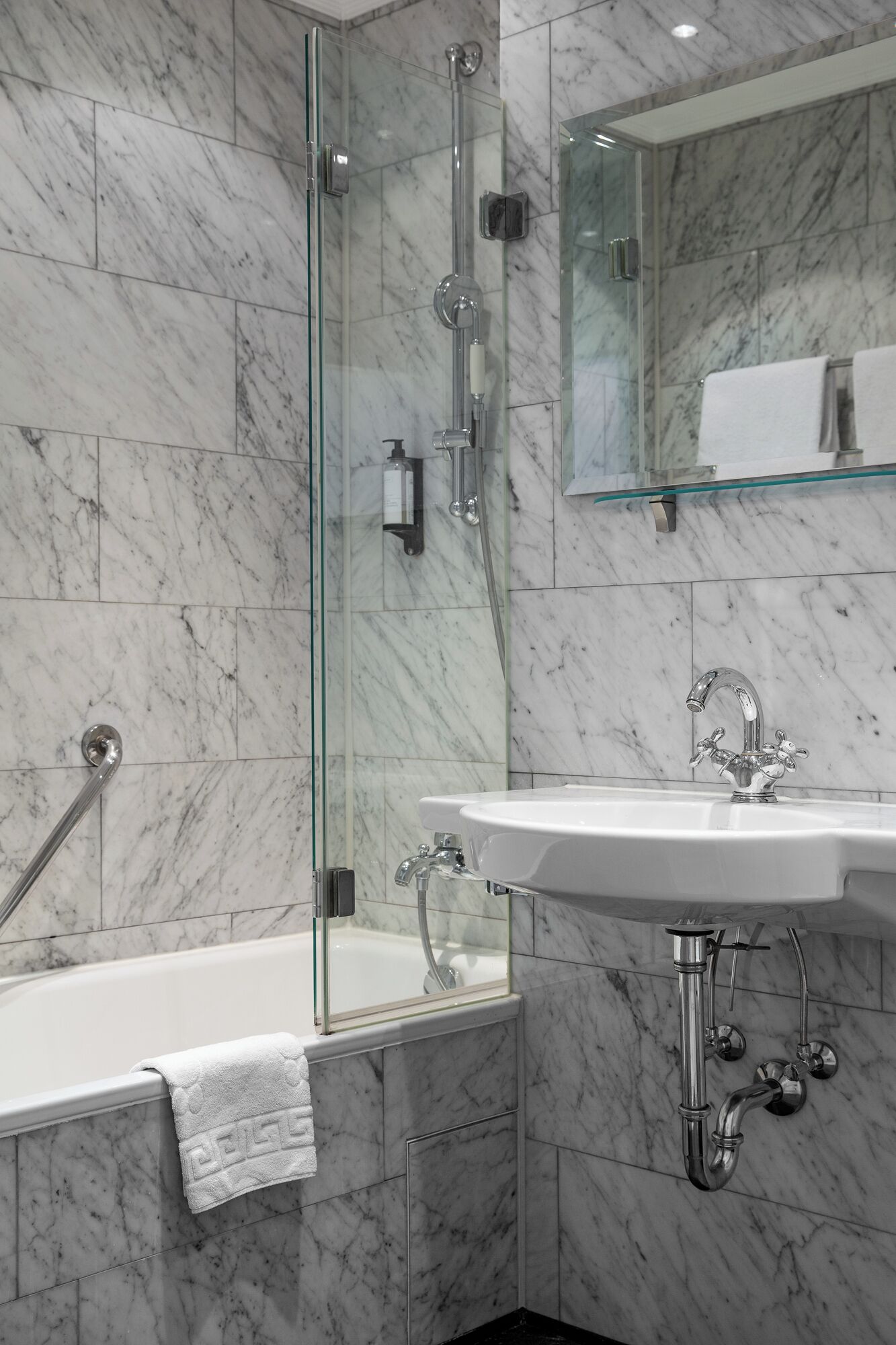 Une salle de bain moderne avec une douche en verre, un lavabo blanc et un mur recouvert de carreaux de marbre.