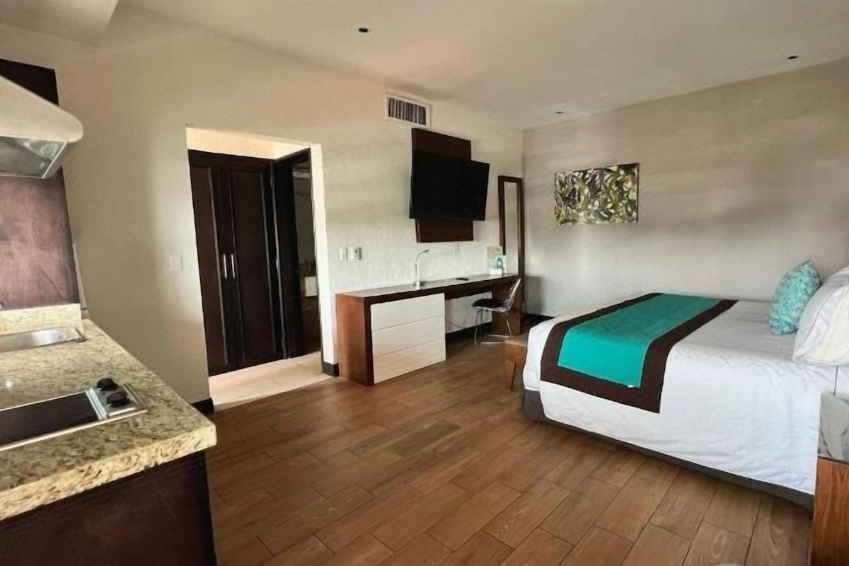 Una habitación de hotel con cama, escritorio, kitchenette y televisión.