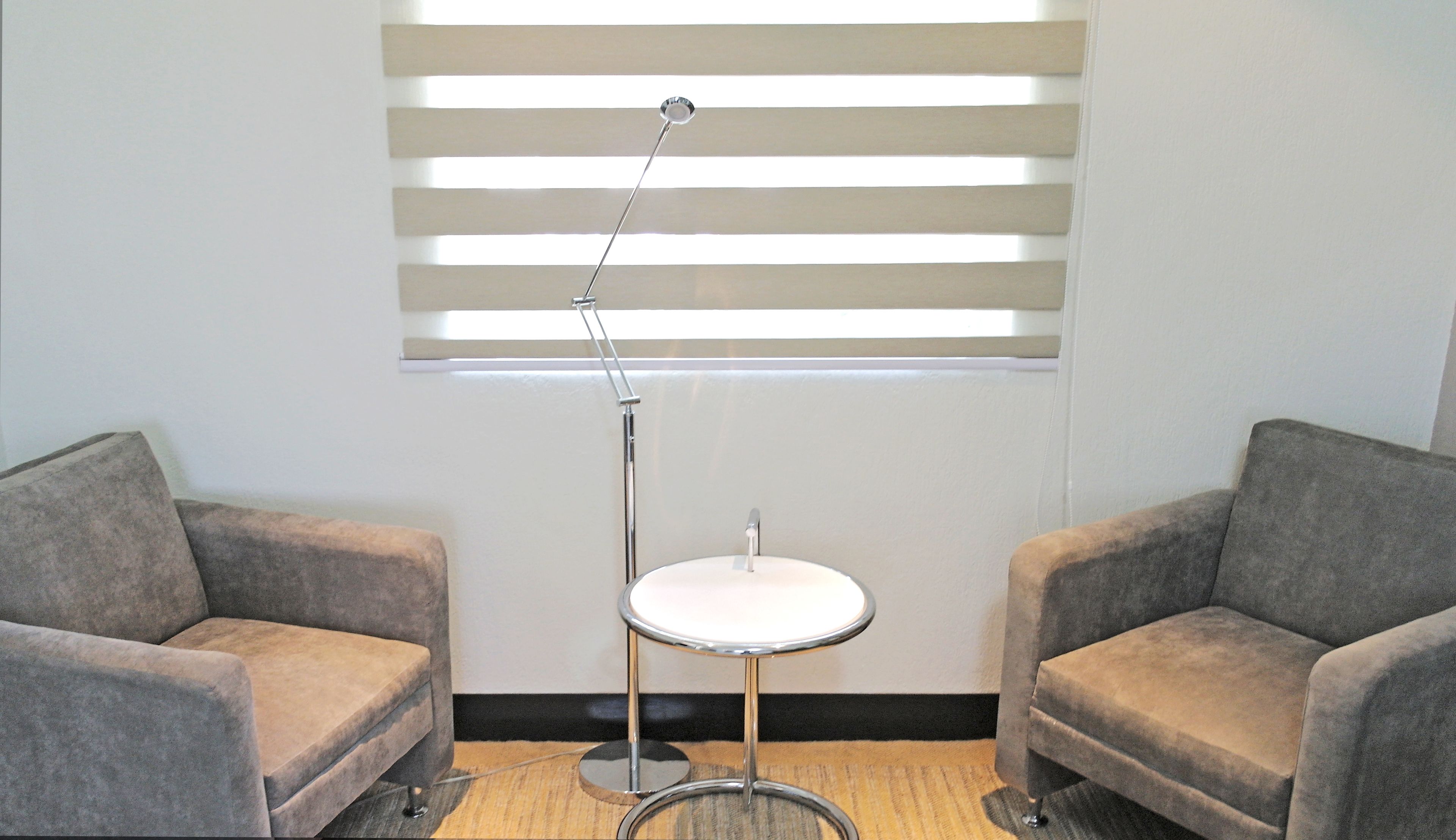 A room with two grey armchairs, a small round table, and a floor lamp.
