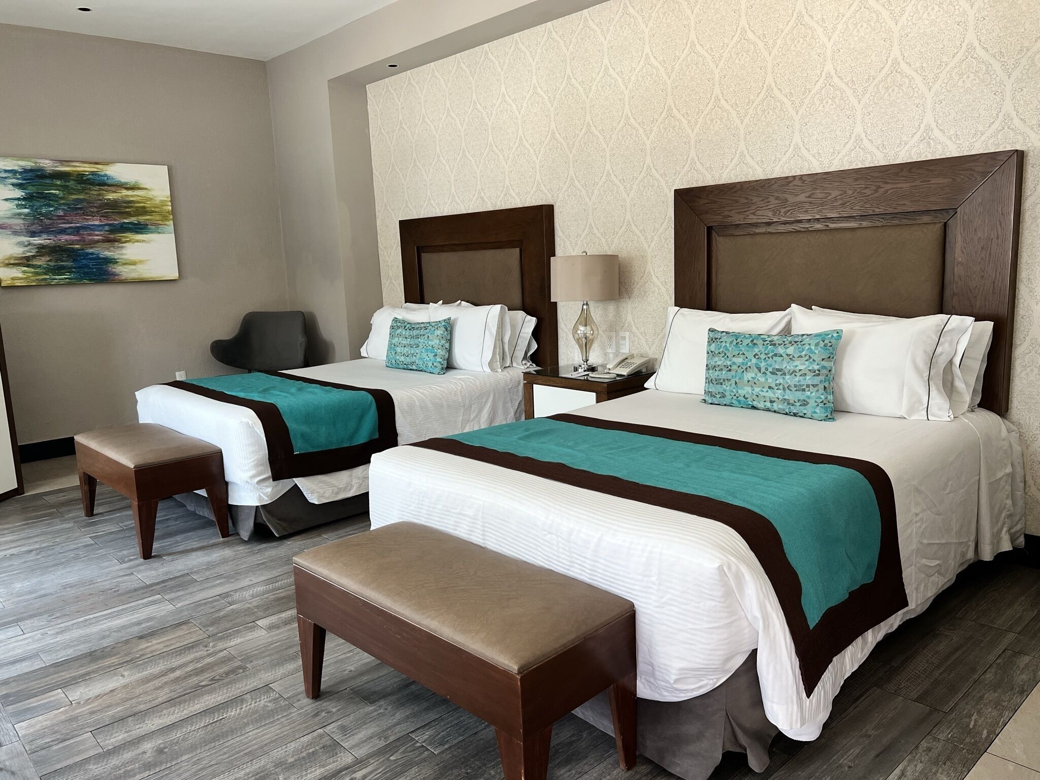 A hotel room with two beds, a desk, a chair, and a bench.