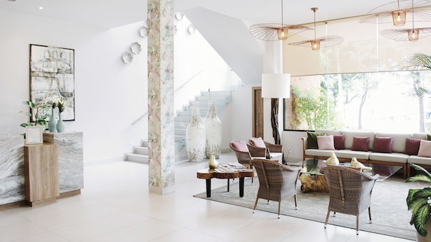 A spacious living area with a marble reception desk, wicker furniture, and a large window overlooking a staircase. - Áurea Hotel & Suites (Zapopan)