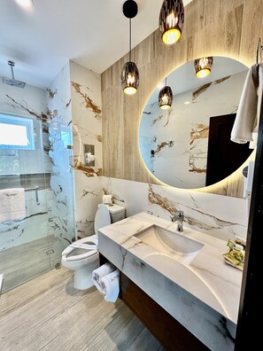 A modern bathroom with a marble vanity, a large mirror, and a glass shower enclosure. - Áurea Hotel & Suites (Zapopan)