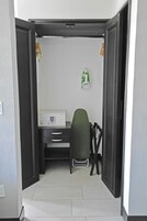 Una habitación pequeña con escritorio, silla y un estante.