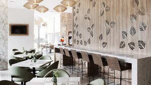 A modern restaurant with a long bar, green chairs, and decorative leaf patterns on the wall. - Áurea Hotel & Suites (Zapopan)