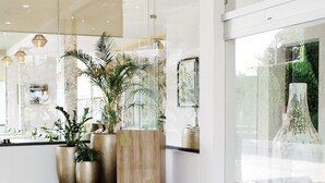 A modern lobby with a curved brick floor, large potted plants, and a large vase on display. - Áurea Hotel & Suites (Zapopan)