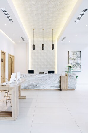 A modern reception area with a marble counter, wooden accents, and pendant lighting. - Áurea Hotel & Suites (Zapopan)