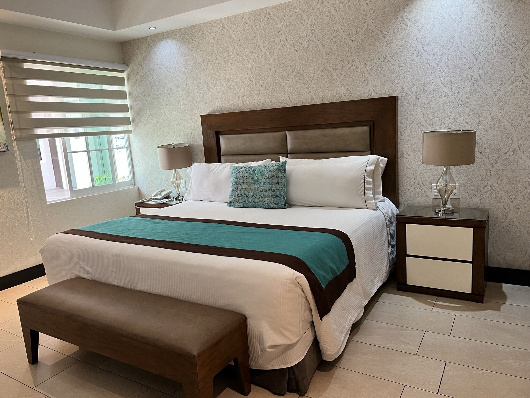 A neatly arranged bedroom with a large bed, bedside lamps, a bench, and a nightstand.