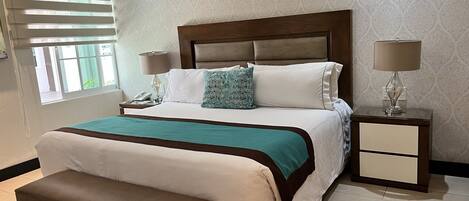 A neatly arranged bedroom with a large bed, bedside lamps, a bench, and a nightstand.