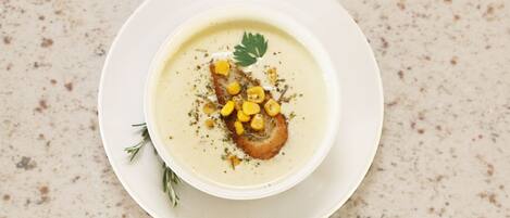 Un plato blanco con una cazuela de sopa, maíz y una guarnición.