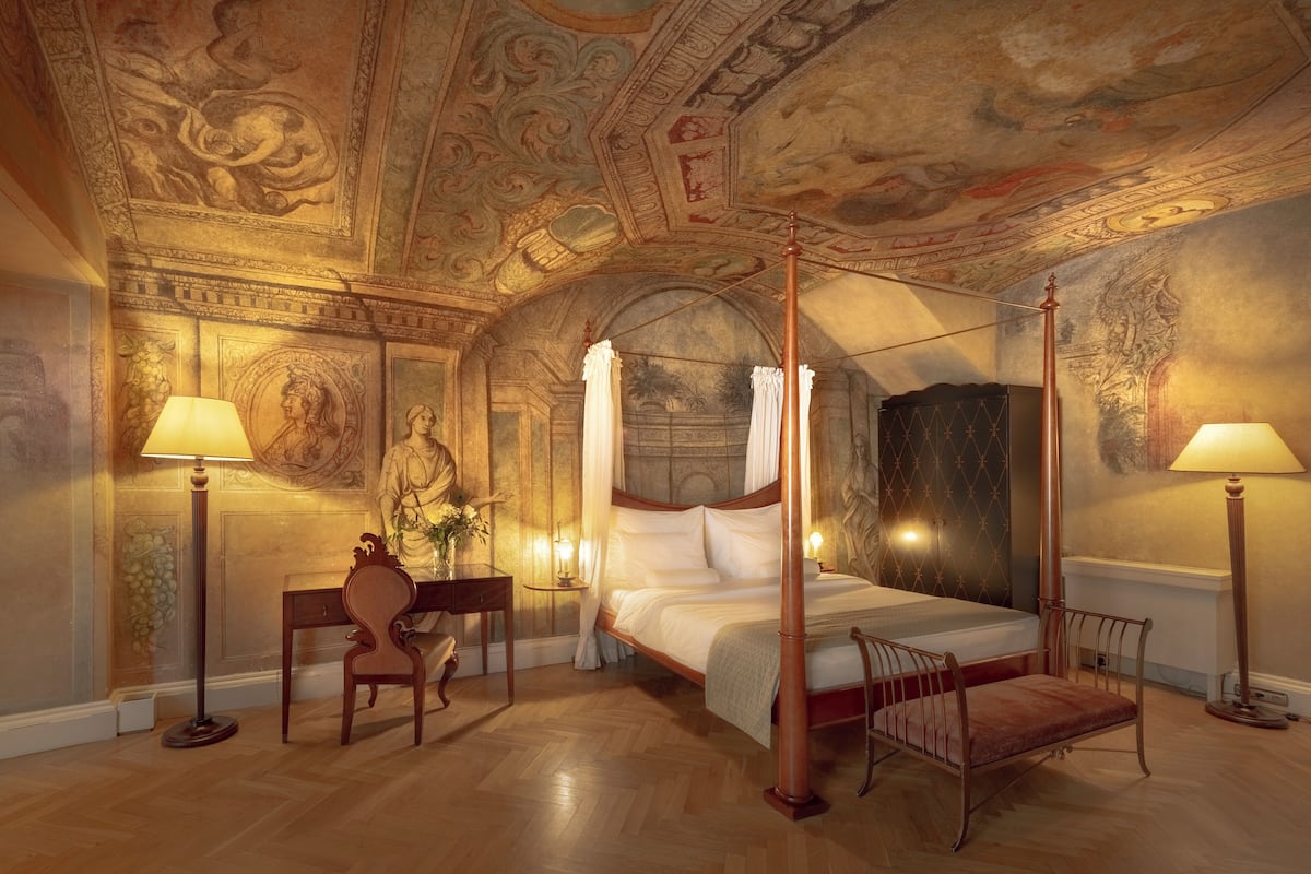 A luxurious bedroom with a four-poster bed, a desk, and a chair.