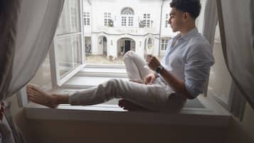 A person sitting by a window with a view of a white building with a red roof.