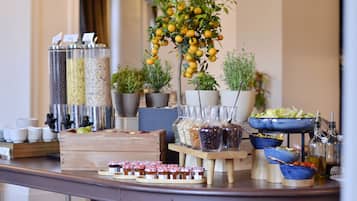A buffet table with various food items, including jars of preserves, a fruit tree, and a bowl of salad.