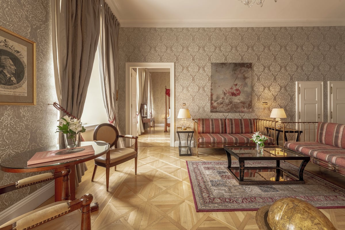 A spacious living room with a patterned wallpaper, a sofa set, a coffee table, and a dining area with a table and chairs.