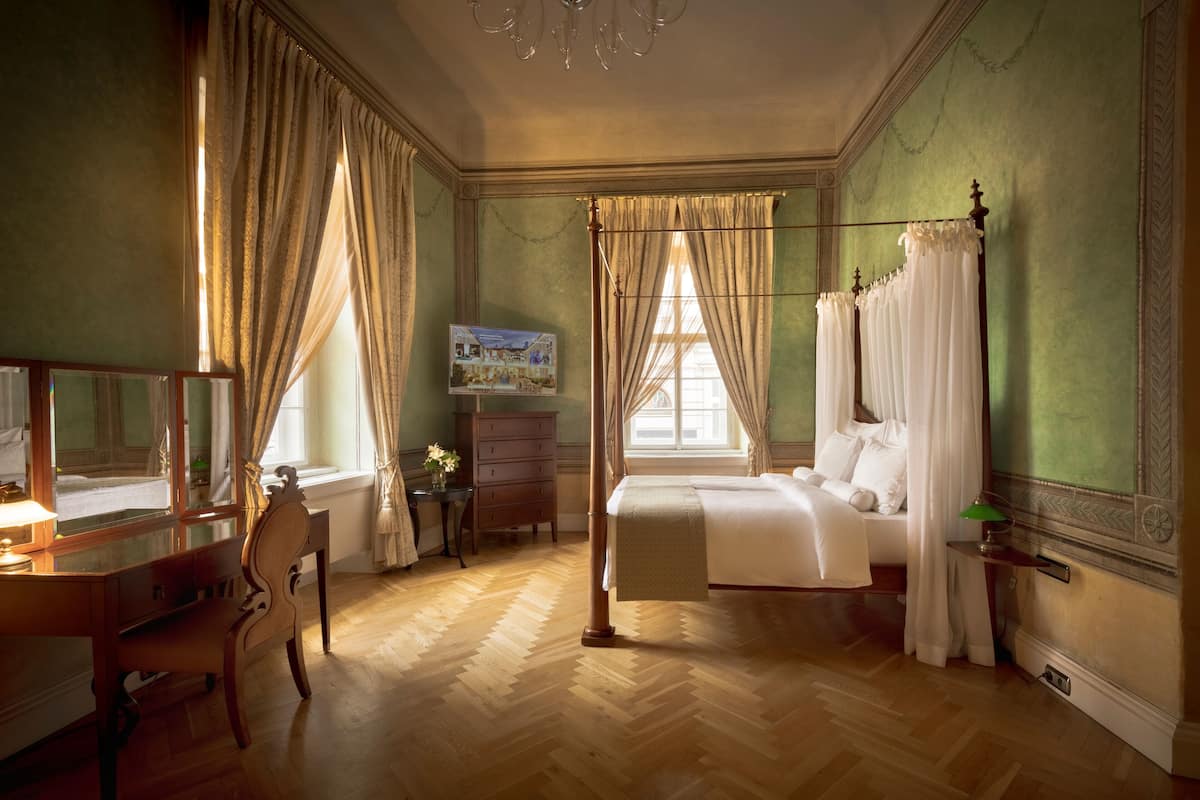 A bedroom with a four-poster bed, a desk with a chair, a dresser, and a window with curtains.