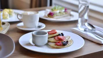 Uma mesa de madeira com panquecas cobertas de morangos e mirtilos, uma chávena de café e um copo de água.
