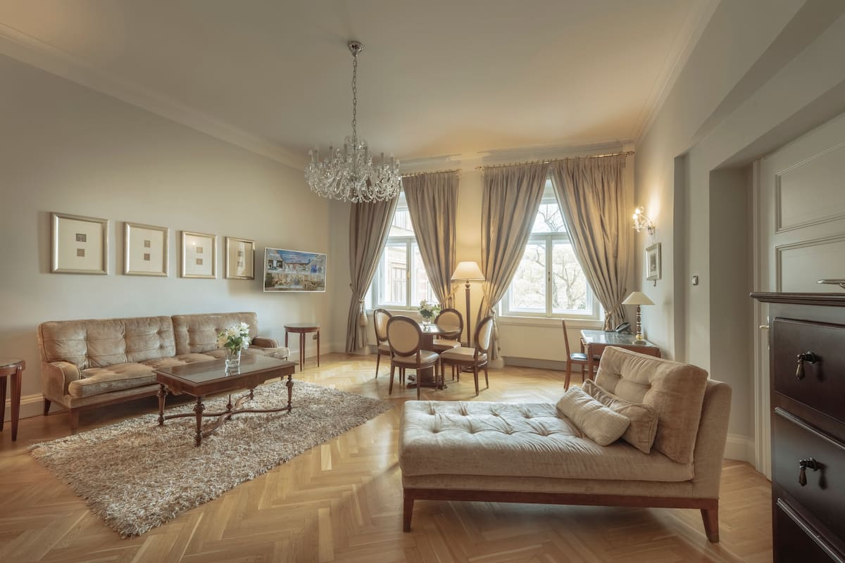 A spacious living room with a sofa, coffee table, and chandelier. There is a dining area with a table and chairs.