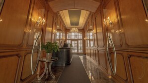 A grand hallway with wooden paneling, a chandelier, and a reception desk with a potted plant. - The Mozart Prague by Accor (Prague)