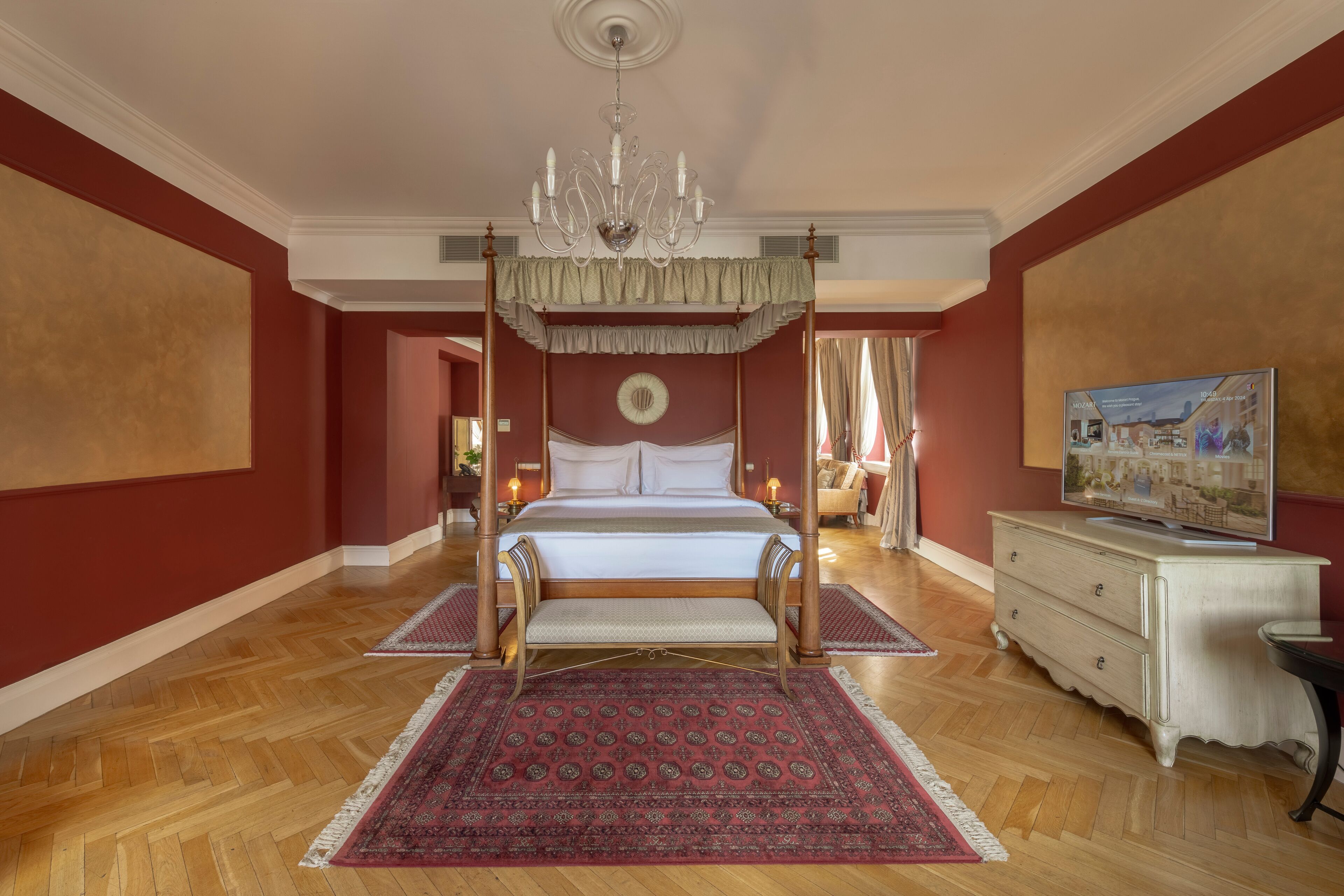 A spacious bedroom with a four-poster bed, a chandelier, a large mirror, and a television on a dresser.