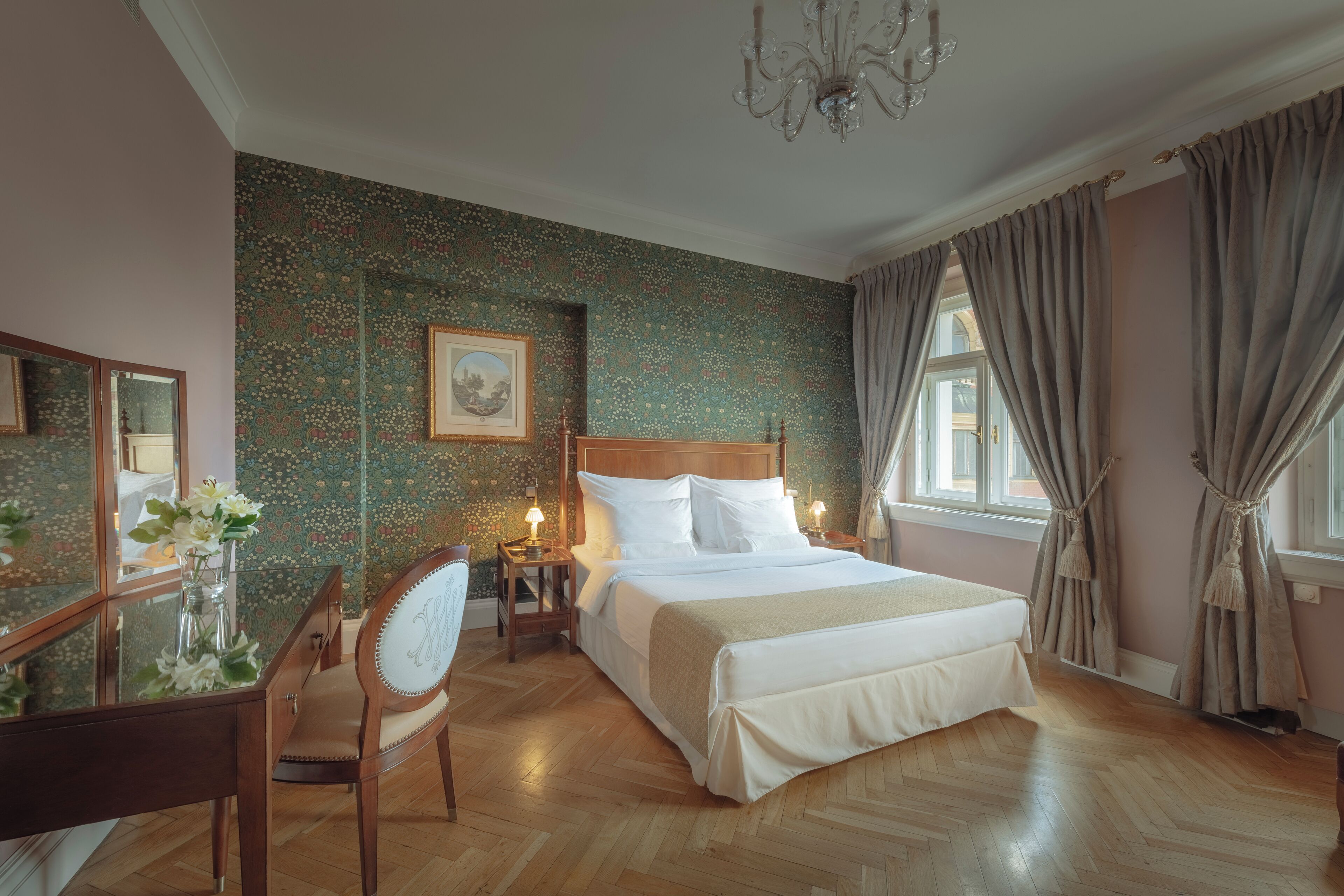 Un dormitorio con una cama de madera, un escritorio con silla, una araña y un ventanal con cortinas.