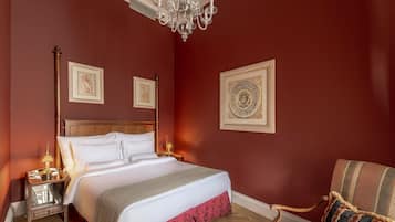 A bedroom with a large bed, a chandelier, and two framed artworks on the wall.