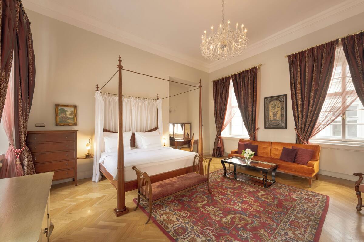 A four-poster bed with a canopy, a wooden bench, a sofa, a coffee table, and a chandelier.